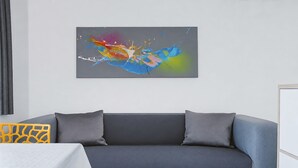 Una sala de estar moderna con un sofá gris, dos cojines grises, un cuadro abstracto y colorido en la pared y una silla amarilla estampada.