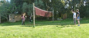 A grassy outdoor area with a volleyball net, trees, and a picnic table.