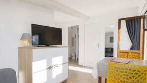 Una habitación de hotel con una televisión sobre un mueble, una mesa con una silla amarilla y un espejo con cortina.