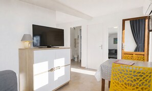 Una camera d'albergo con televisione su un mobile, un tavolo con una sedia gialla e uno specchio con tenda.