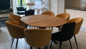 Un comedor moderno con una mesa redonda de madera y seis sillas, una lámpara colgante y vistas al exterior a través de amplios ventanales.