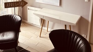 Una habitación moderna con un escritorio blanco, dos sillones de cuero negro, un cuadro grande de montañas en la pared y un cartel que dice "APRES-SKI".
