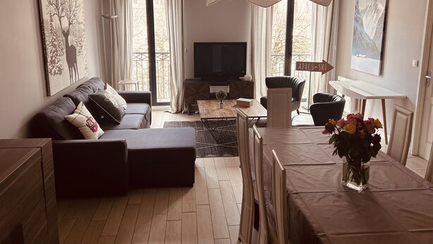 Una sala de estar moderna con un sofá, una mesa de comedor con sillas, un televisor y obras de arte en las paredes.