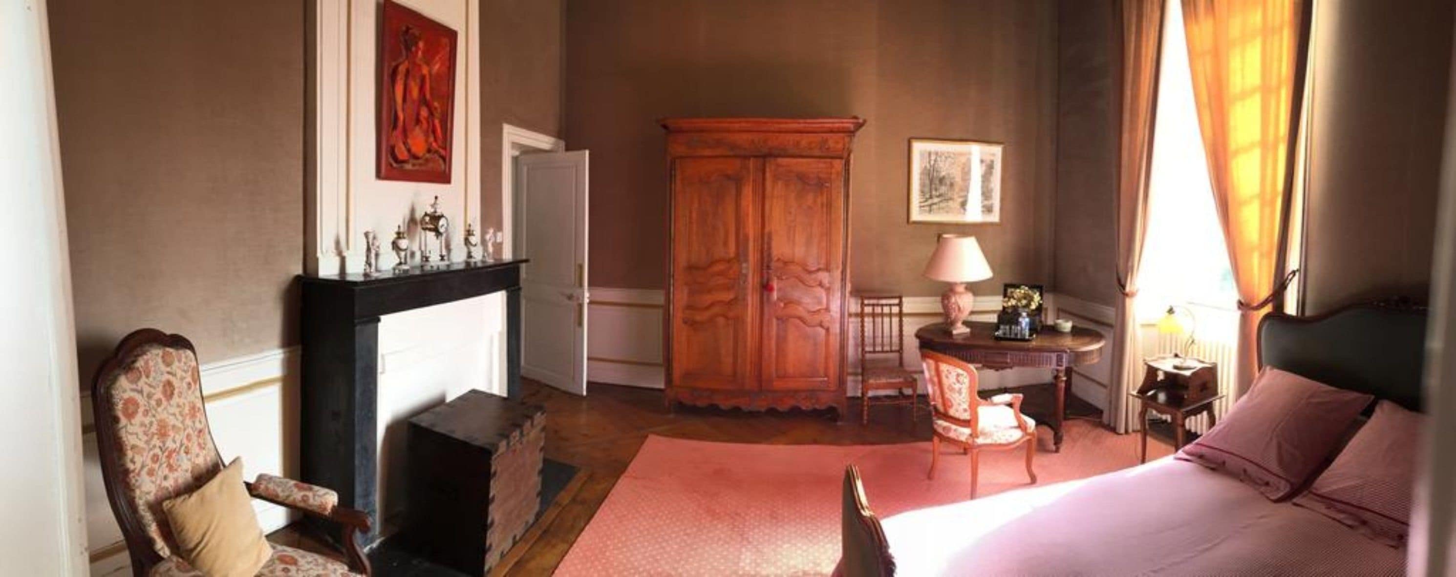 Quarto com cama, poltrona, mesa, armário e lareira.