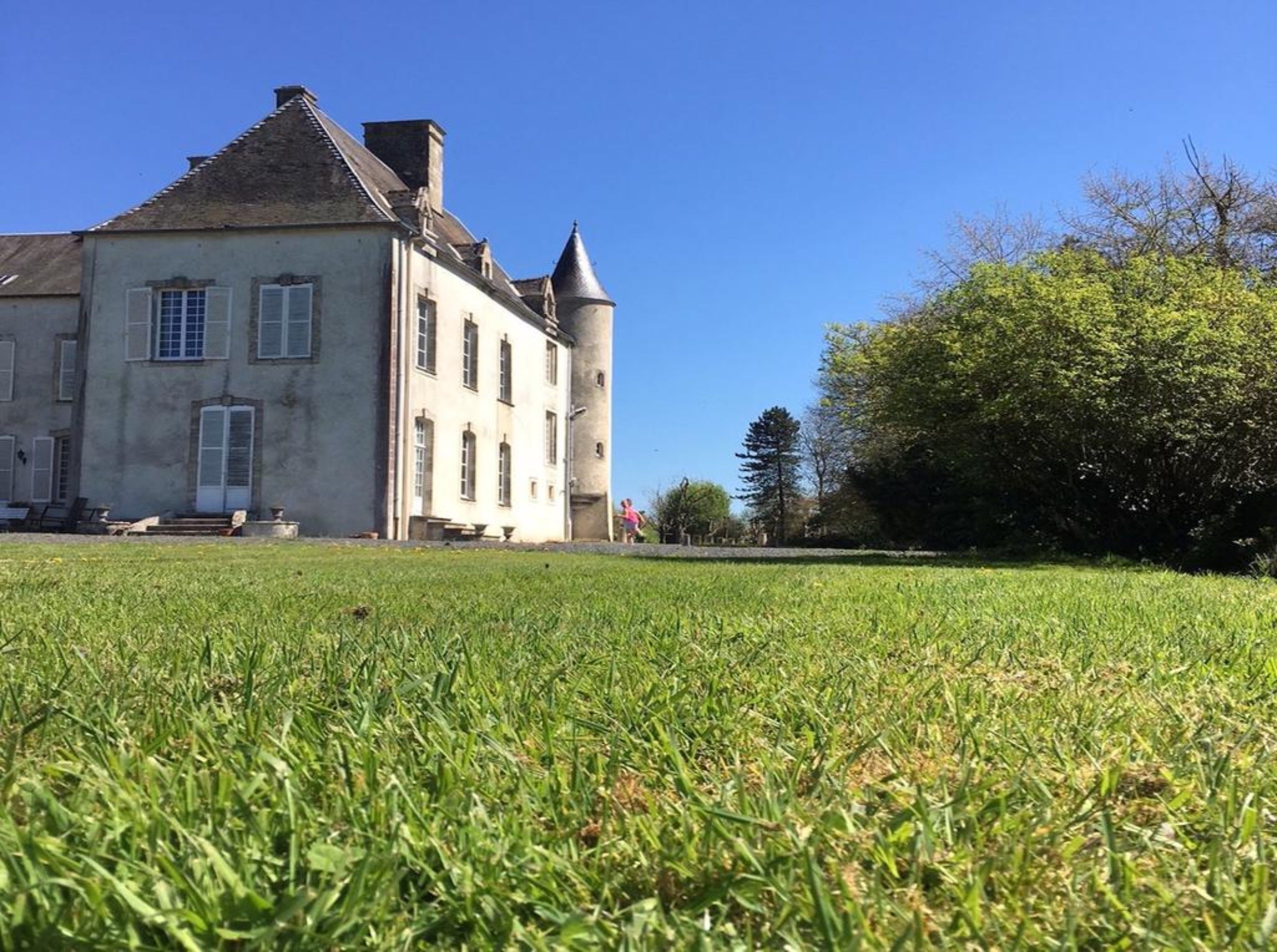 Un grand bâtiment historique, doté d’une tour imposante et de fenêtres disposées de manière symétrique, et entouré d’une pelouse bien entretenue.