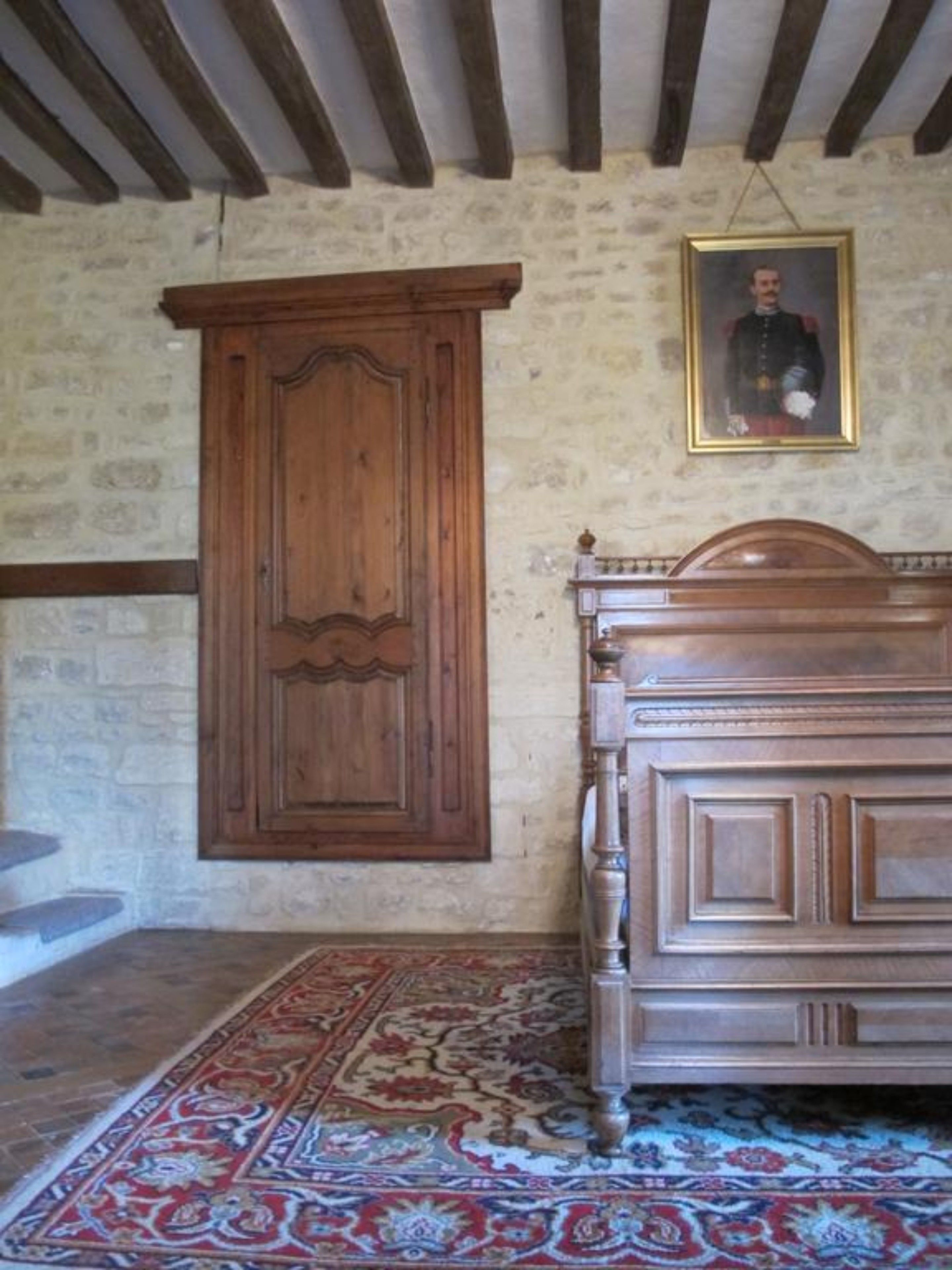Una stanza con un'armadietto in legno, un letto con testiera, un tappeto decorato e un ritratto incorniciato appeso al muro.