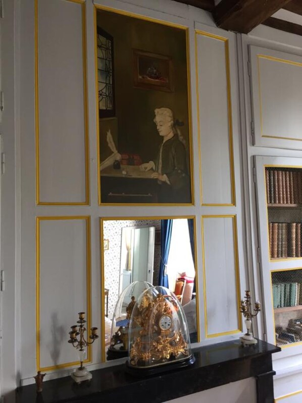 A room with a fireplace, a framed picture above it, and a bookshelf to the right. - Château d'Asnieres en Bessin (Asnieres-en-Bessin)