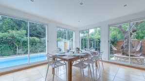A dining area with a large table and chairs, large windows with a view of a swimming pool and greenery. - Villa Olivier with a private pool—10 minutes from the beach (Bompas)
