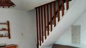 Un escalier avec des rampes en bois, un canapé marron avec des coussins rouges, un meuble en bois et un luminaire suspendu.
