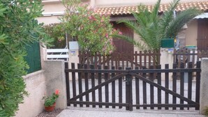 Une entrée fermée par un portail, avec un chemin en béton menant à un bâtiment doté d’un toit en tuiles.