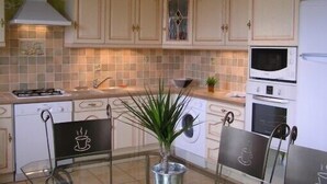 A kitchen with white cabinets, a microwave, oven, and a stove. There is a plant on the counter and a chair with a cup design.