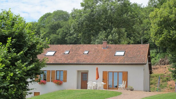 A two-story house with a tiled roof, wooden shutters, and a small patio with outdoor furniture.