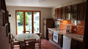A kitchen with a dining table and chairs, a refrigerator, oven, dishwasher, and a window overlooking a garden. -  ... Charming Residence in the heart of Gascony, with Jacuzzi & sauna (Estipouy)