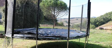 Un trampolín con red de seguridad, rodeado de césped y árboles.