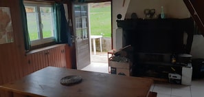 A rustic kitchen with a wooden table, a window with curtains, and a view of a garden. - Ideal for hikers (Laruns)