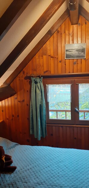 A bedroom with a sloped ceiling, wooden walls, a window with curtains, and a bed with a quilt. - Ideal for hikers (Laruns)