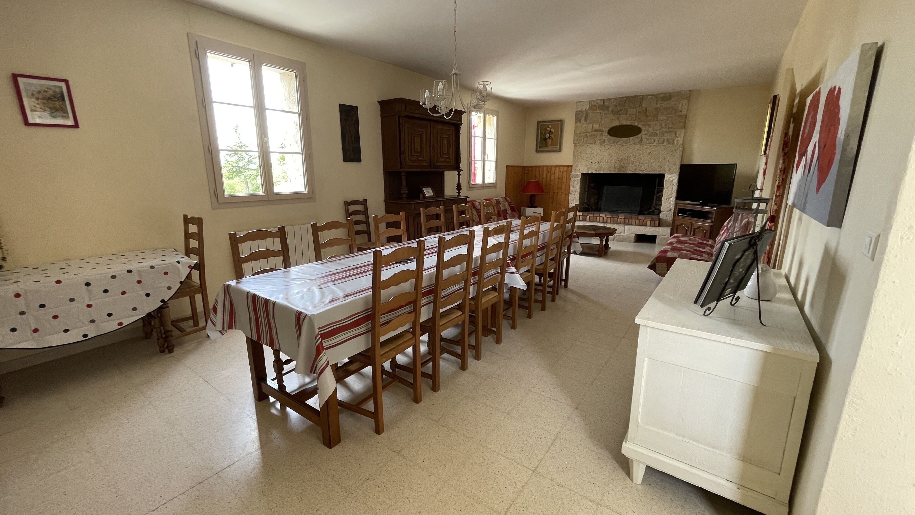 A dining area with a long table and chairs, a fireplace, and a television.