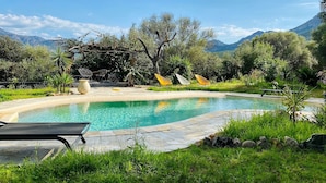 Une piscine d’un bleu éclatant, agrémentée de chaises longues et d’une pergola, le tout entouré de verdure et avec des montagnes en toile de fond.