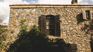 Un bâtiment en pierre à l’aspect rustique, doté d’une porte en bois et de volets aux fenêtres.