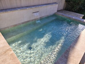 Une piscine aux eaux cristallines, bordée de pierres, agrémentée d’un élément décoratif aquatique et dotée d’une avancée en pierre.