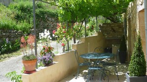 Un patio al aire libre con una mesa y sillas, rodeado de plantas en macetas y un muro de piedra.