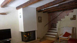 Una sala de estar con chimenea, televisor, mesa de madera, sofá rojo y una escalera.
