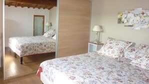 Un dormitorio con dos camas, vigas de madera, un espejo, una mesita de noche con lámpara y un adorno floral en la pared.