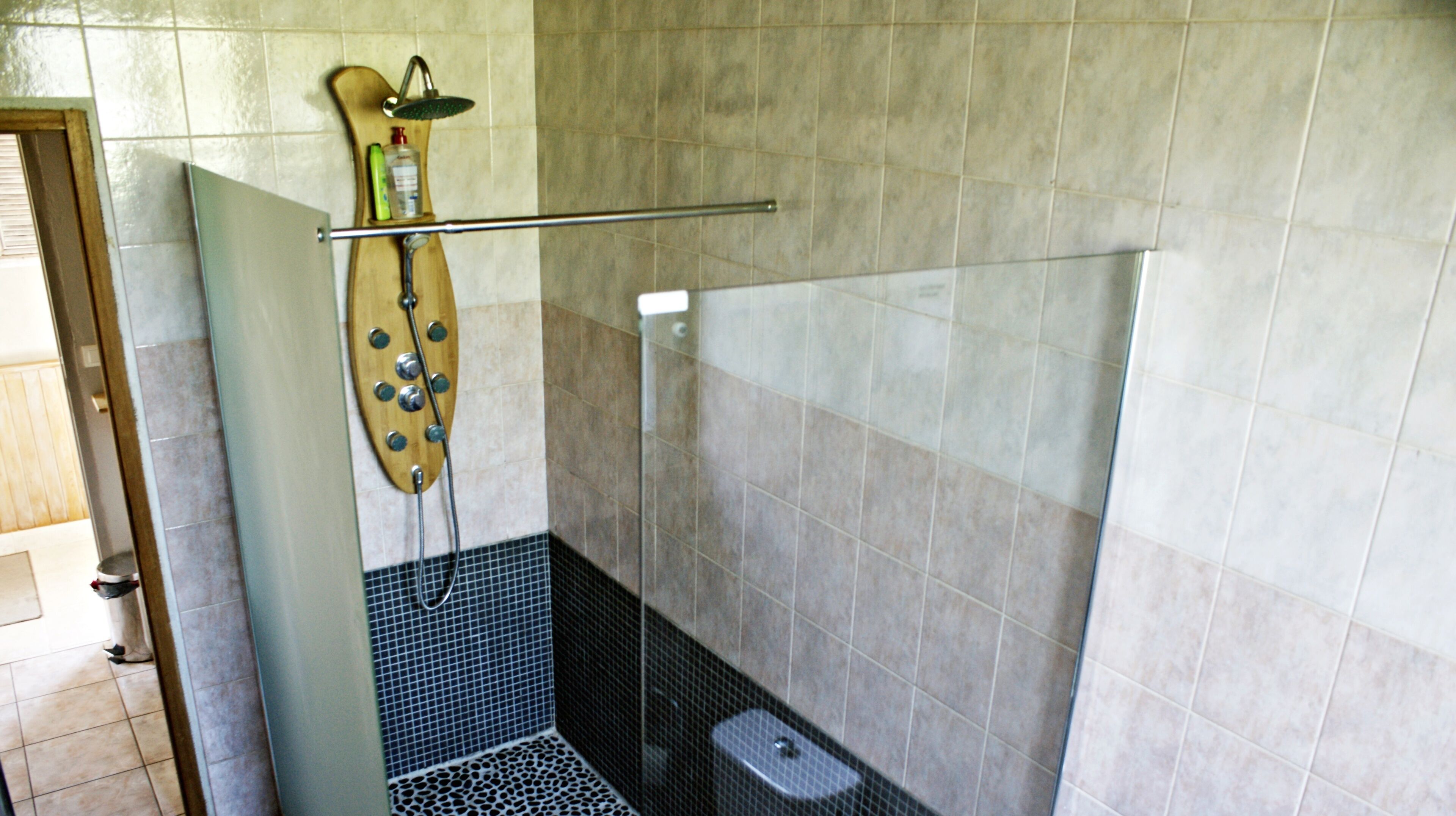 Une douche avec un panneau en bois, une porte en verre et des murs carrelés.