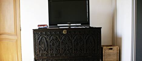 Un mueble de madera oscura con intrincados grabados, un televisor de pantalla plana encima y una pequeña cesta de mimbre a su lado.