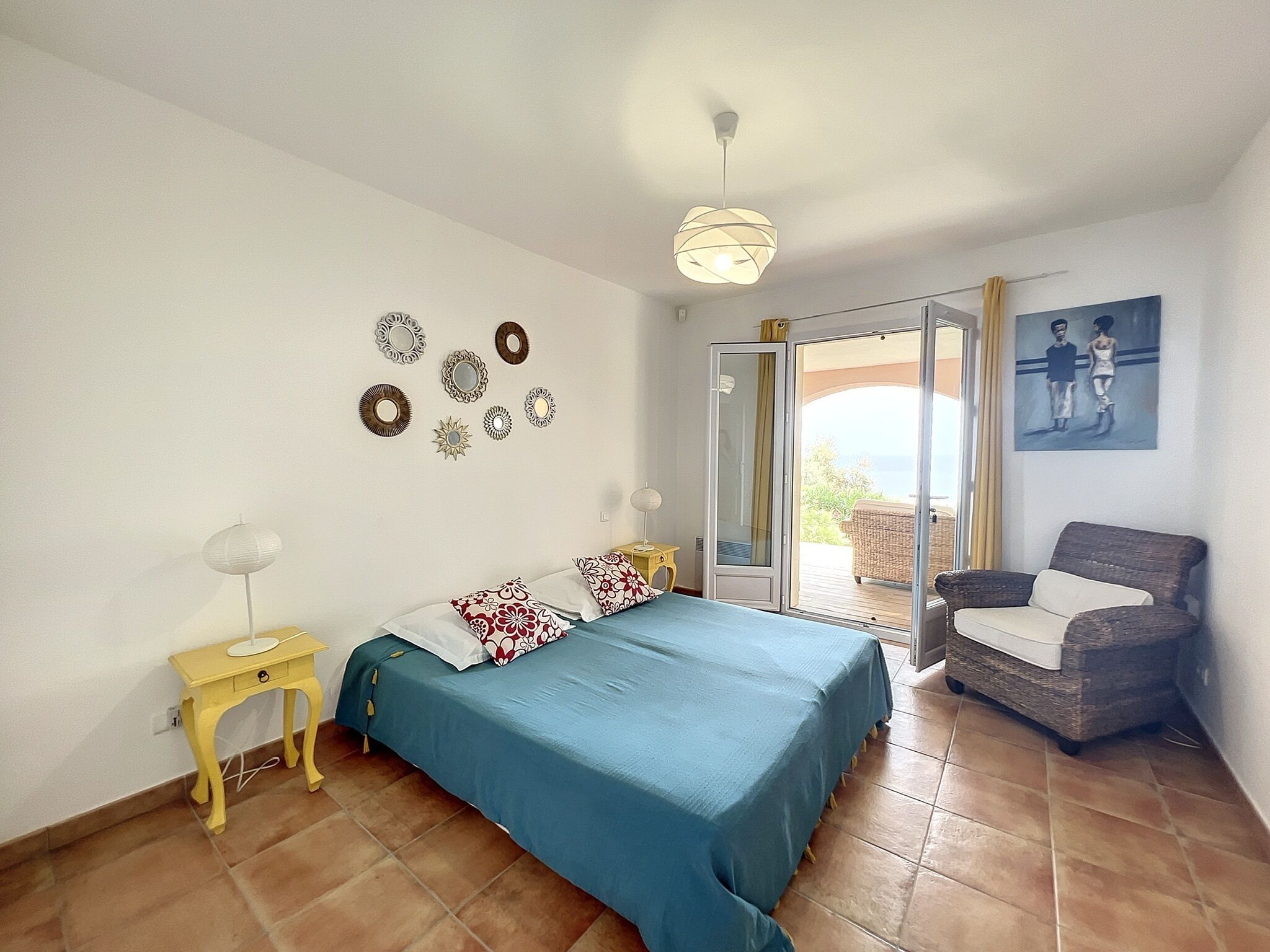 A bedroom with a bed, a chair, a table, and a balcony with a view.