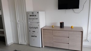 A modern living room with a white refrigerator, a wooden cabinet, a flat-screen TV mounted on the wall, and a small table with two lemons. - Diamond Beachfront Studio (Le Diamant)
