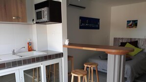 A compact kitchen with a microwave, sink, and stools. - Diamond Beachfront Studio (Le Diamant)