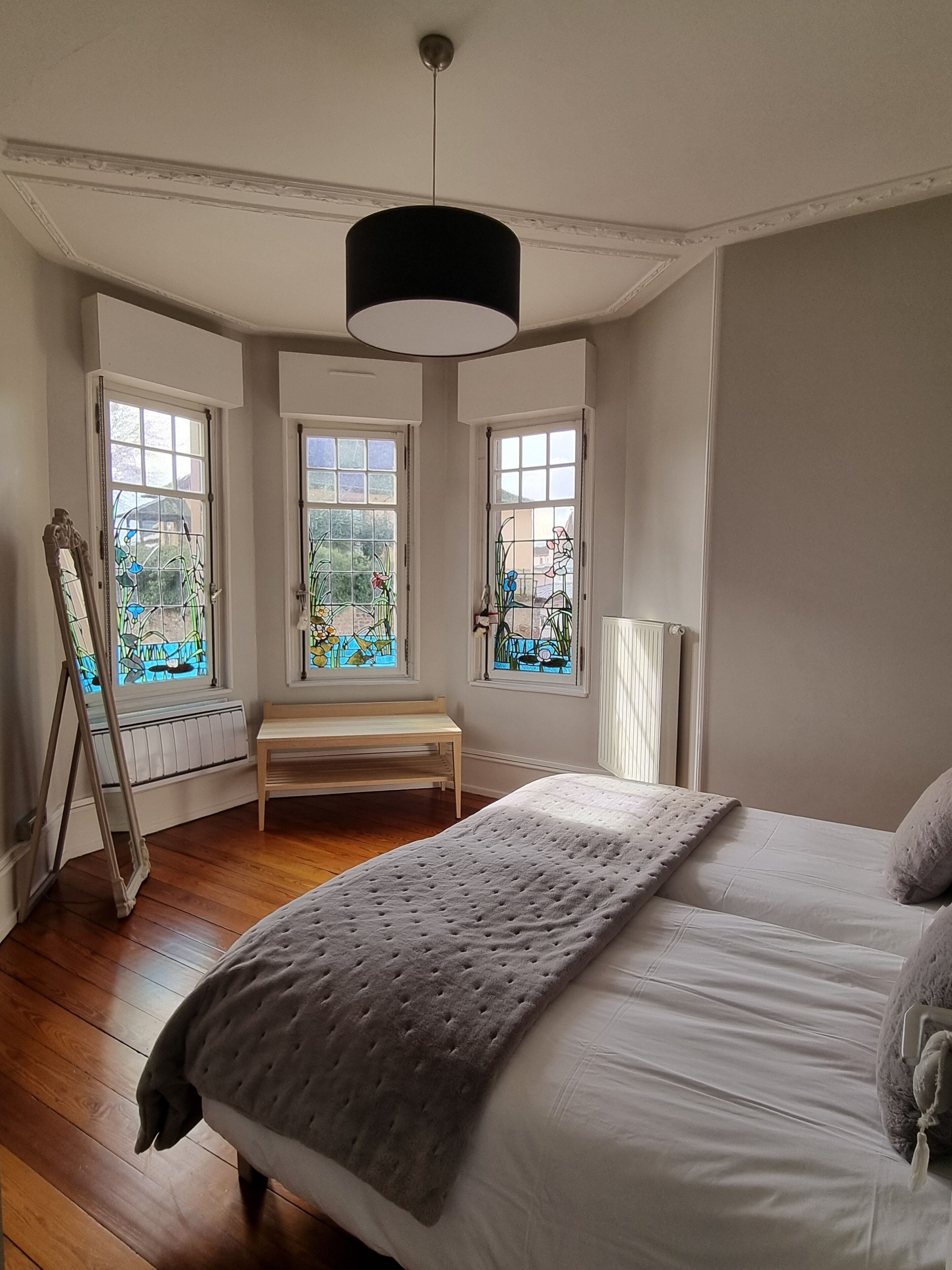 A bedroom with a large bed, a bench, and three windows with stained glass.