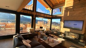 A modern living room with a large sofa, a coffee table, and a fireplace. There are multiple windows offering a view of the mountains. - Chalet Aguila 5***** (NEW) sleeps 12 - XXL. jacuzzi and panoramic sauna (Bolquère)