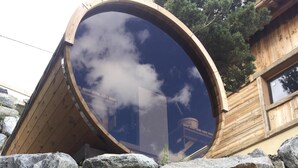 A circular wooden structure with a reflective surface, surrounded by large rocks and grass. - Chalet Aguila 5***** (NEW) sleeps 12 - XXL. jacuzzi and panoramic sauna (Bolquère)