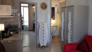 Un salon moderne avec un canapé rouge, un meuble blanc et un coin cuisine comprenant un réfrigérateur et une lampe.