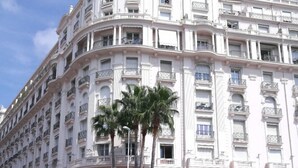 Un grand hôtel blanc, à plusieurs étages, doté de balcons, de palmiers et d’une structure moderne en verre à l’avant.