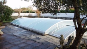 Une serre dotée d’une toiture incurvée, entourée d’une terrasse dallée et d’un mur en pierre.