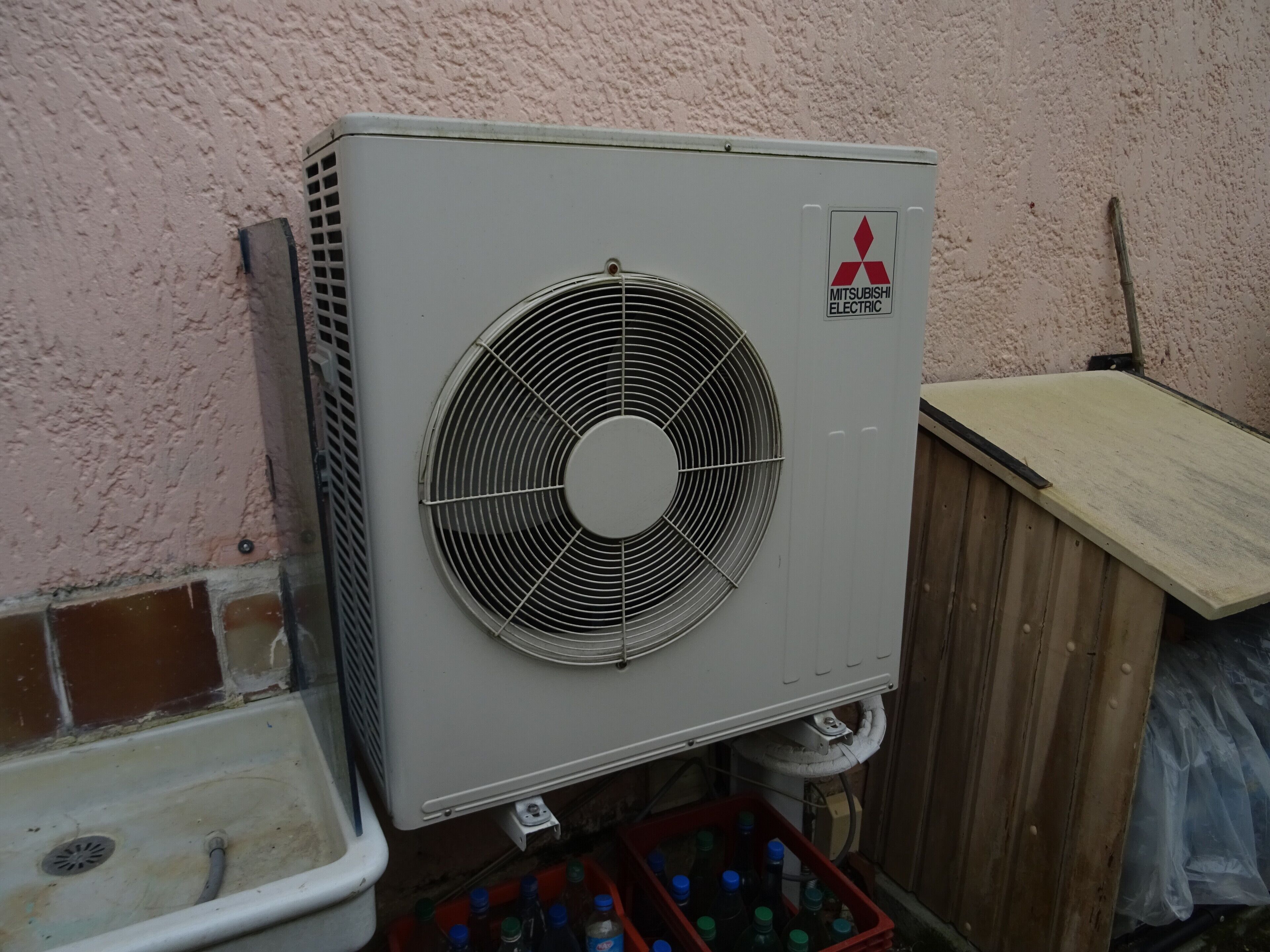 Un appareil de climatisation Mitsubishi Electric fixé au mur, avec une structure en bois à proximité.