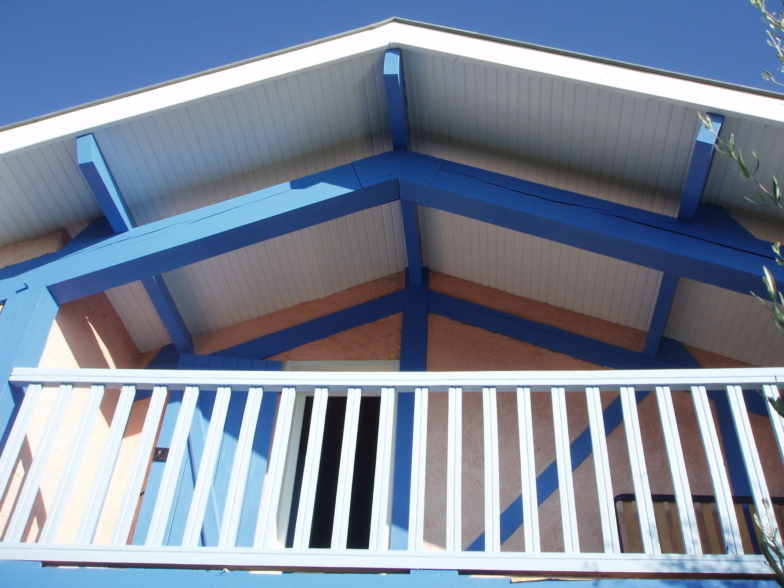 A building with a blue and white color scheme, featuring a balcony with white railings and a blue roof structure.