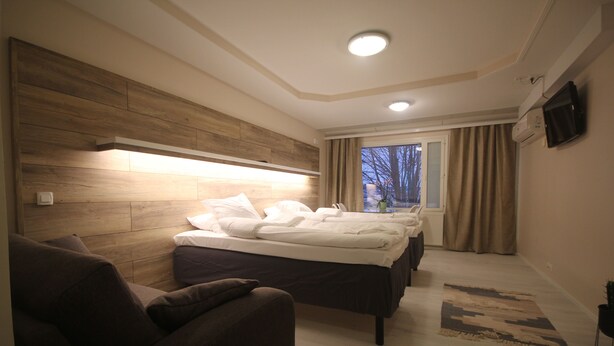 A modern hotel room with a large bed, a sofa, a flat-screen TV, and a window with curtains. - Huoneistohotelli Jääskän Loma (Kauhava)