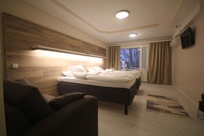 Ein modernes Hotelzimmer mit einem großen Bett, einem Schlafsofa, einem Flachbildfernseher und einem Fenster mit Vorhängen.