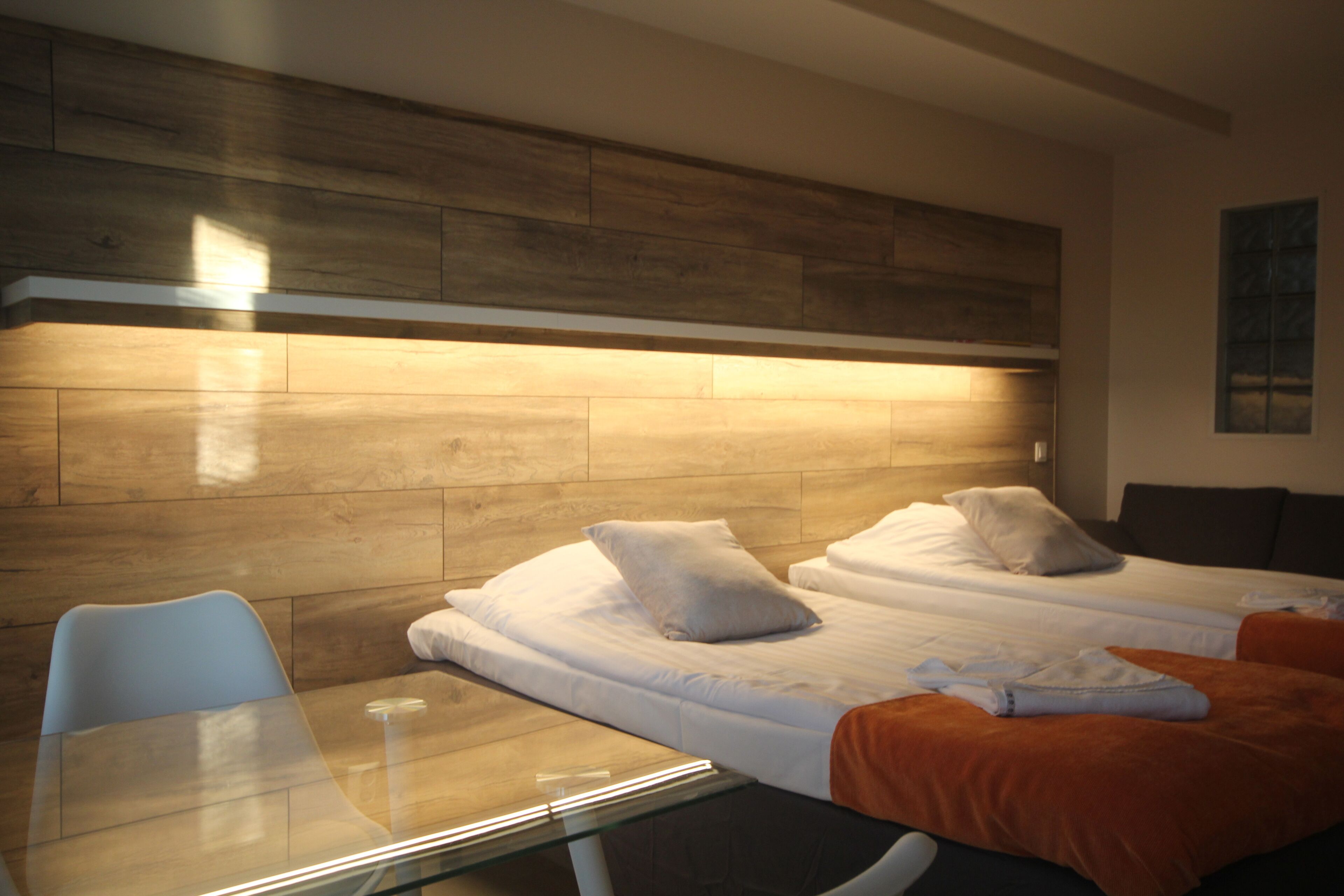 A hotel room with two beds, a glass table, and a wooden headboard.