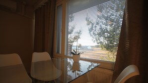 A room with a glass table and white chairs, a window with blinds, and a potted plant on the table. - Huoneistohotelli Jääskän Loma (Kauhava)