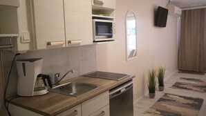 A modern kitchen with a coffee maker, sink, and microwave. There are potted plants and a TV mounted on the wall. - Huoneistohotelli Jääskän Loma (Kauhava)