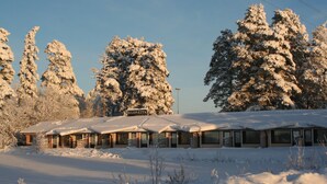 A snow-covered building with a sign reading "HUON EITA" in a snowy landscape with tall trees. - Huoneistohotelli Jääskän Loma (Kauhava)