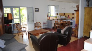 A spacious living room with a sofa, chairs, and a dining area. A kitchen with a window and a sink is visible in the background. - Charming Gites in Provence, with pool  (Vaison-La-Romaine)