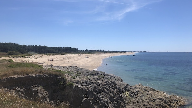 Un paisaje costero con una playa arenosa, afloramientos rocosos y un cielo azul despejado.