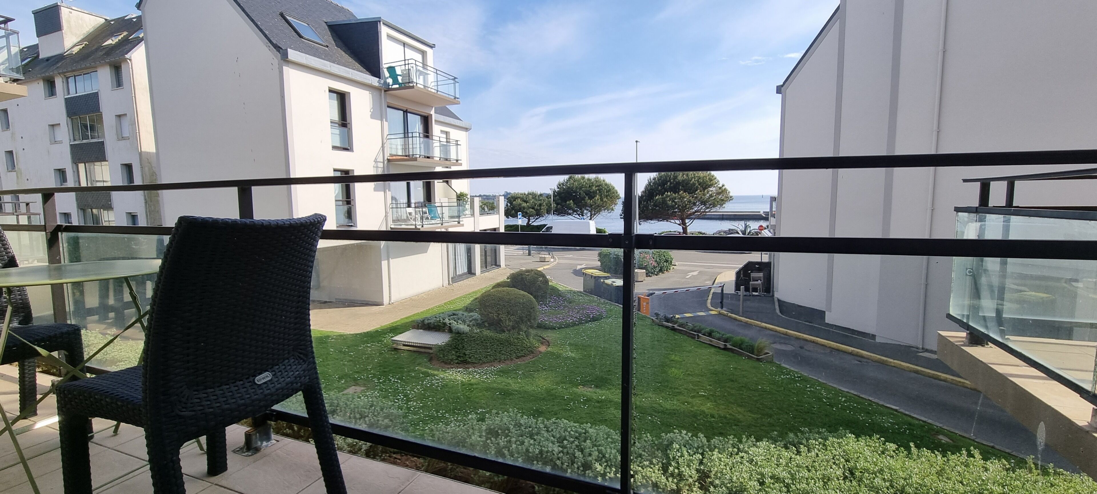 Ein Balkon mit Korbstuhl, Blick auf einen gepflegten Garten und moderne Gebäude im Hintergrund.