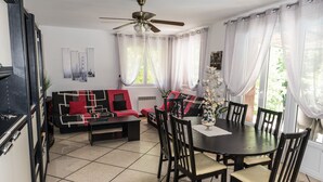 A dining area with a round table and chairs, a sofa with red cushions, and a ceiling fan. - Riverfront house with pool at the foot of the Cascades du Sautadet (La Roque-Sur-Cèze)